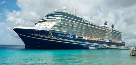 A side view of the Celebrity Equinox cruise ship docked at a pier, surrounded by clear turquoise waters under a cloudy sky.