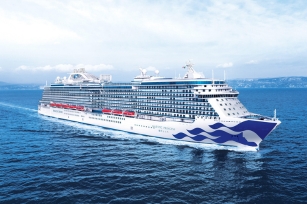 Image of the cruise ship gliding through the clear blue waters featuring clouds in the backdrop