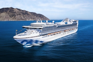 Aerial image of the Star Princess cruise ship from the front with mountains in the background as the cruise ship glides through the deep blue waters